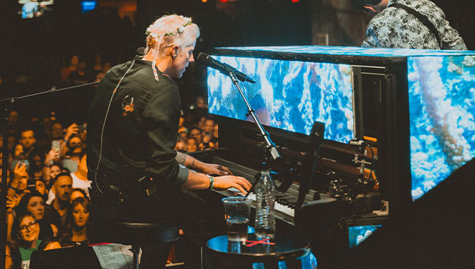 A person playing a piano with LED video walls attached to it